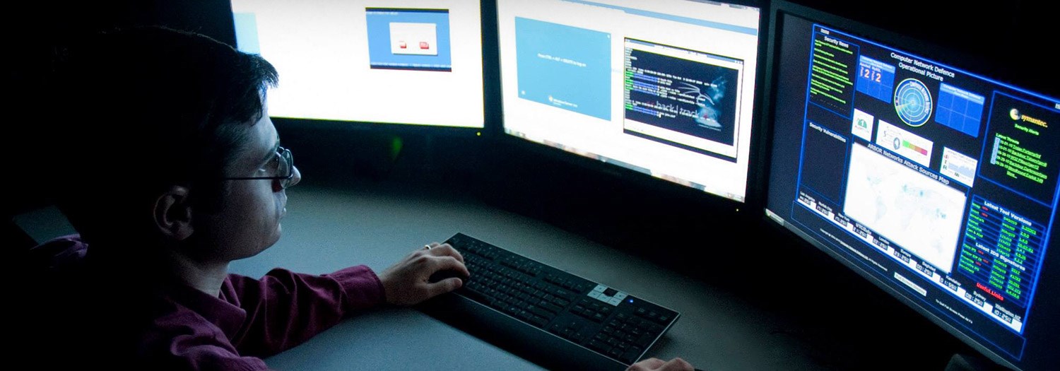 Student seated at a bank of three computer screens