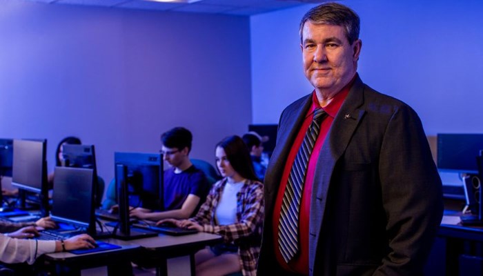 Ken Dewey poses for a picture in front of Cybersecurity students. 