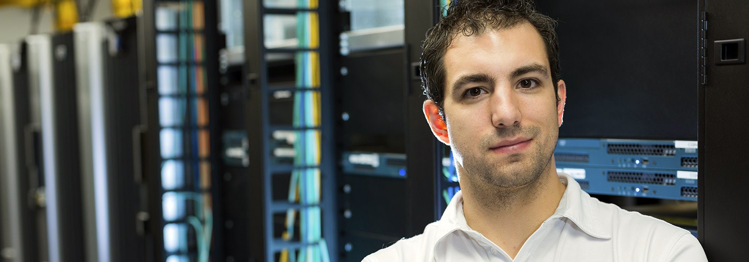 Student standing before a bank of network devices in a tower.