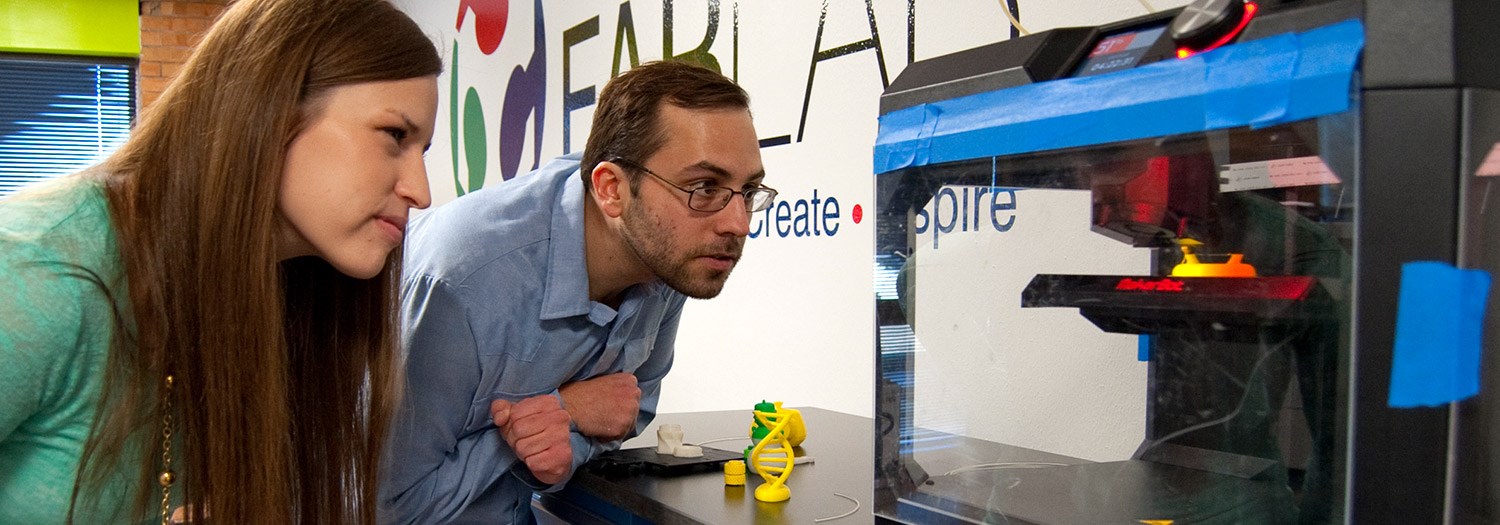 Two students watching a 3D printer in the FabLab