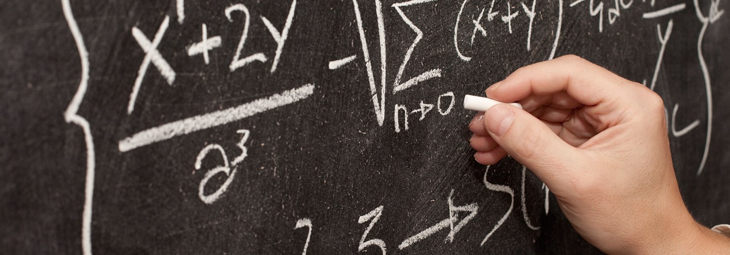 Closeup of hand writing equations with chalk on a blackboard.