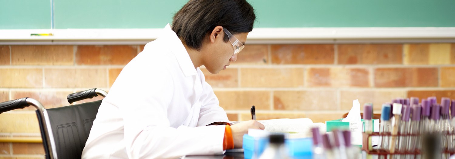 male student making notes surrounded by test tubes