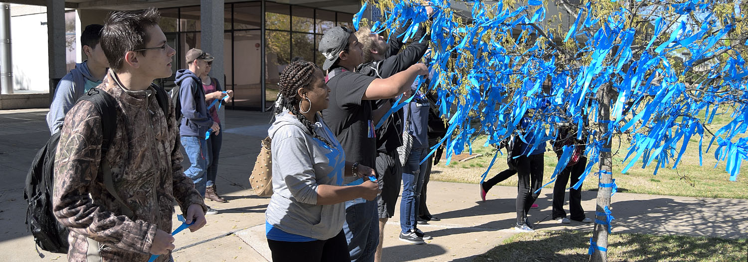 Students placing blue ribbons on a tree on campus.