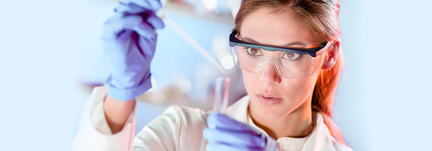 Woman in lab coat putting substance into testing tube.