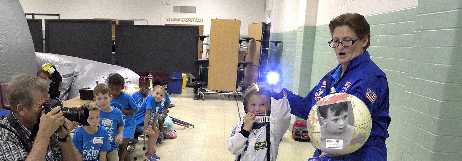 Young Kid’s College student dressed in astronaut suit using a flashlight shining on the earth to explain night and day.